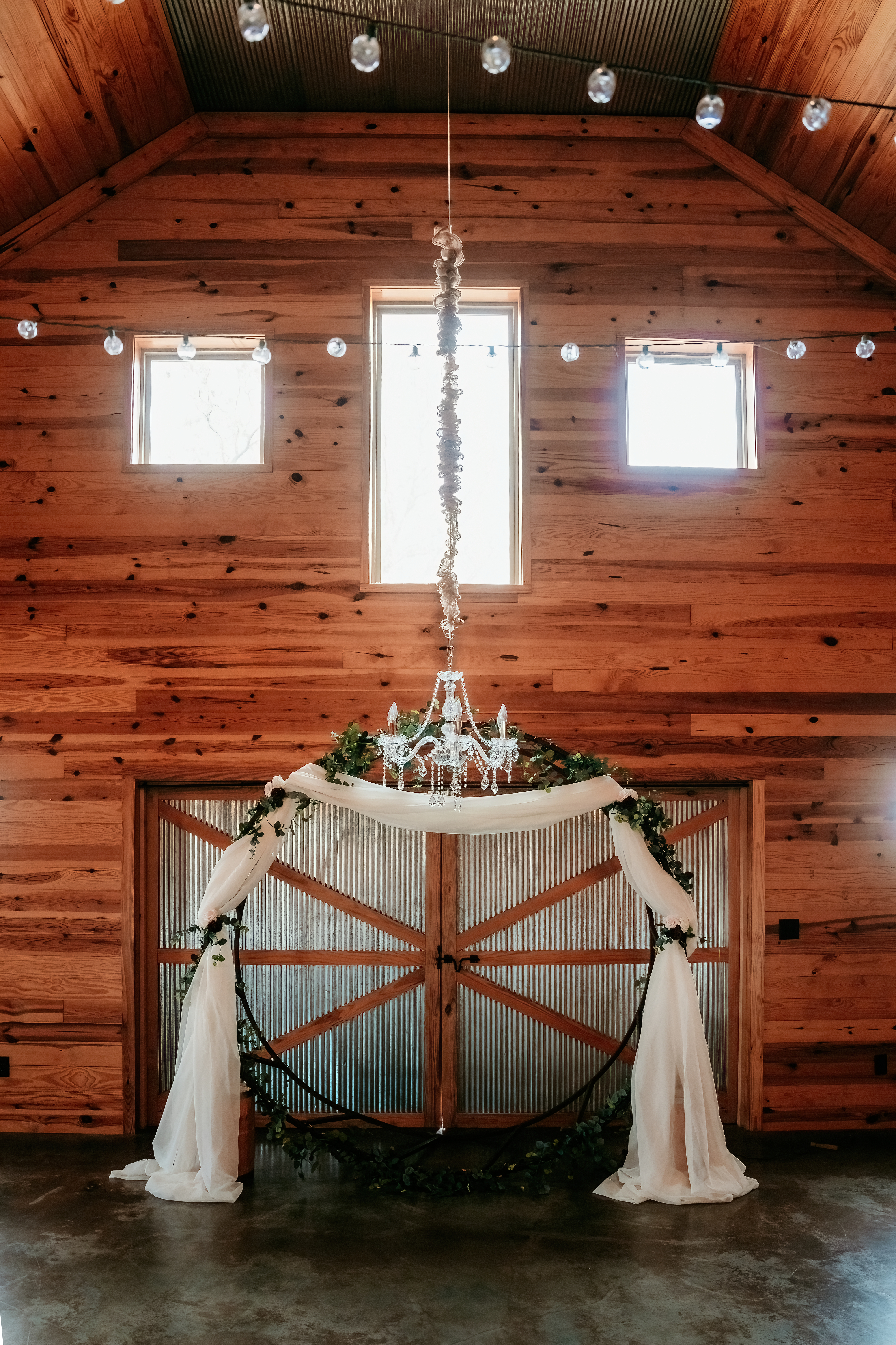 round wedding arch with white drapery and greenery under chandelier
